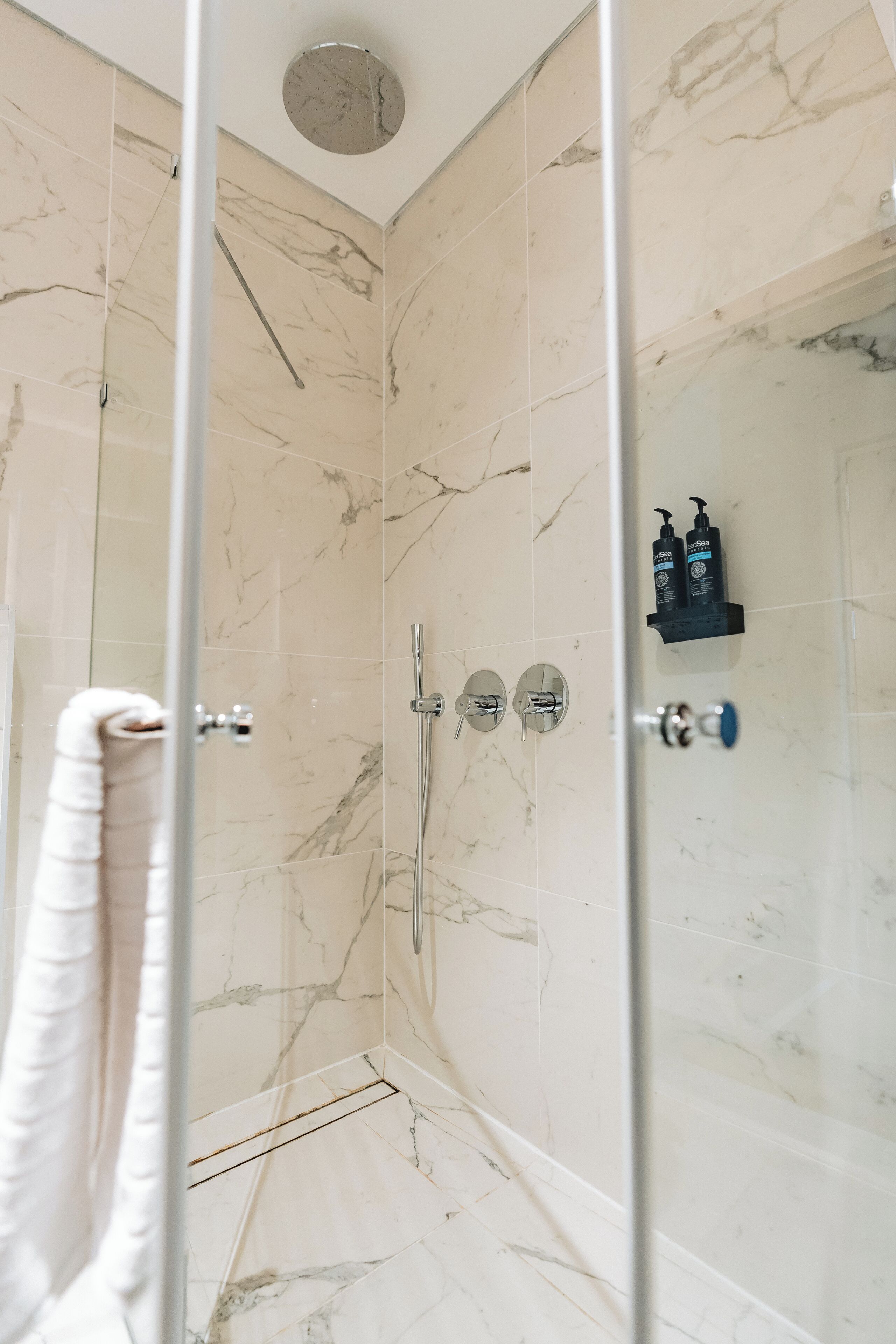 A modern bathroom with marble tiles, a glass shower enclosure, and a towel rack.