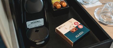 Una bandeja con una caja de bombones Almena, una cafetera y un juego de cápsulas de café.