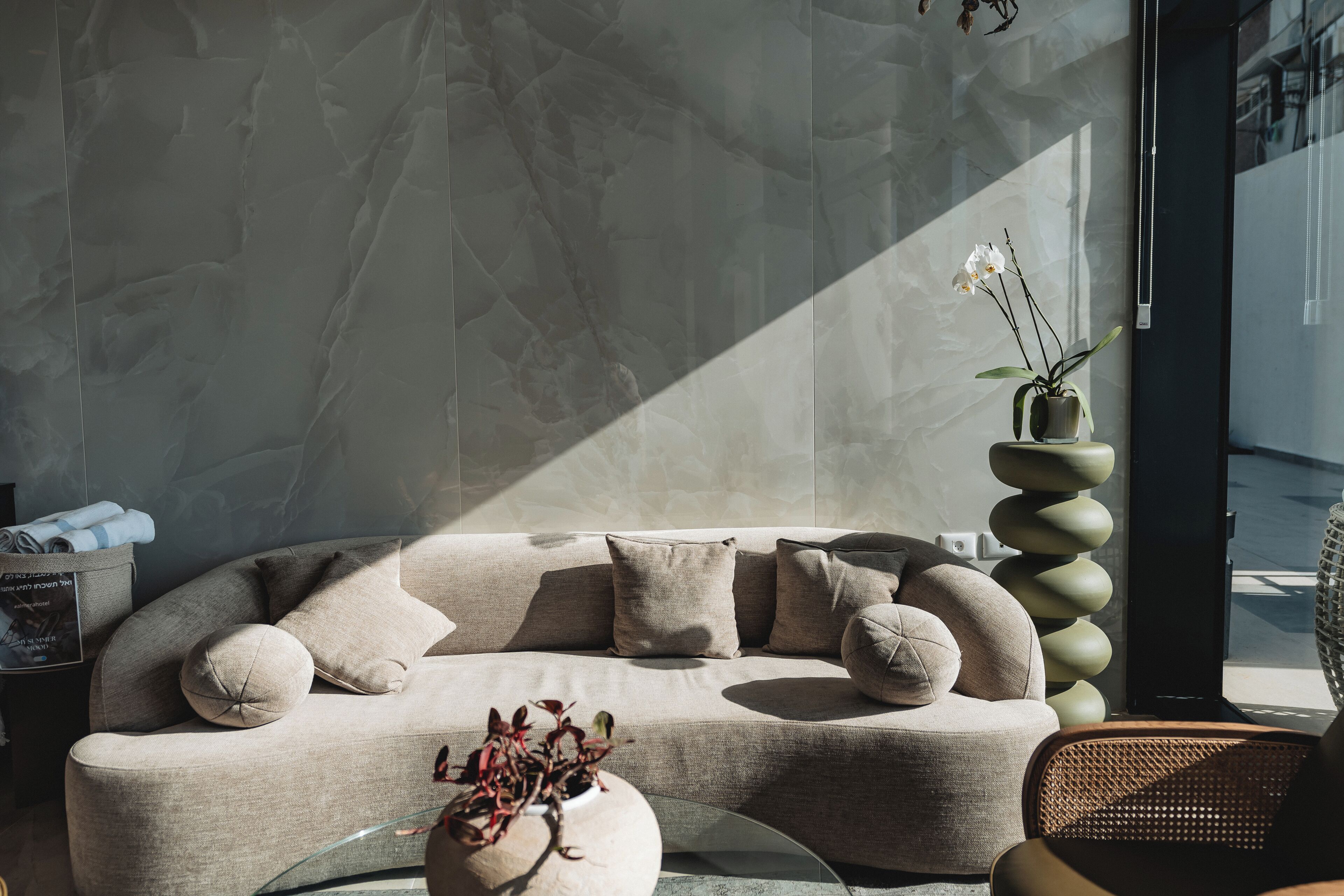A modern living room with a curved sofa, a round coffee table, and a tall, spiral planter with flowers.