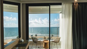 Una habitación con un amplio ventanal corredizo que da a un balcón con vista a la playa y al océano.