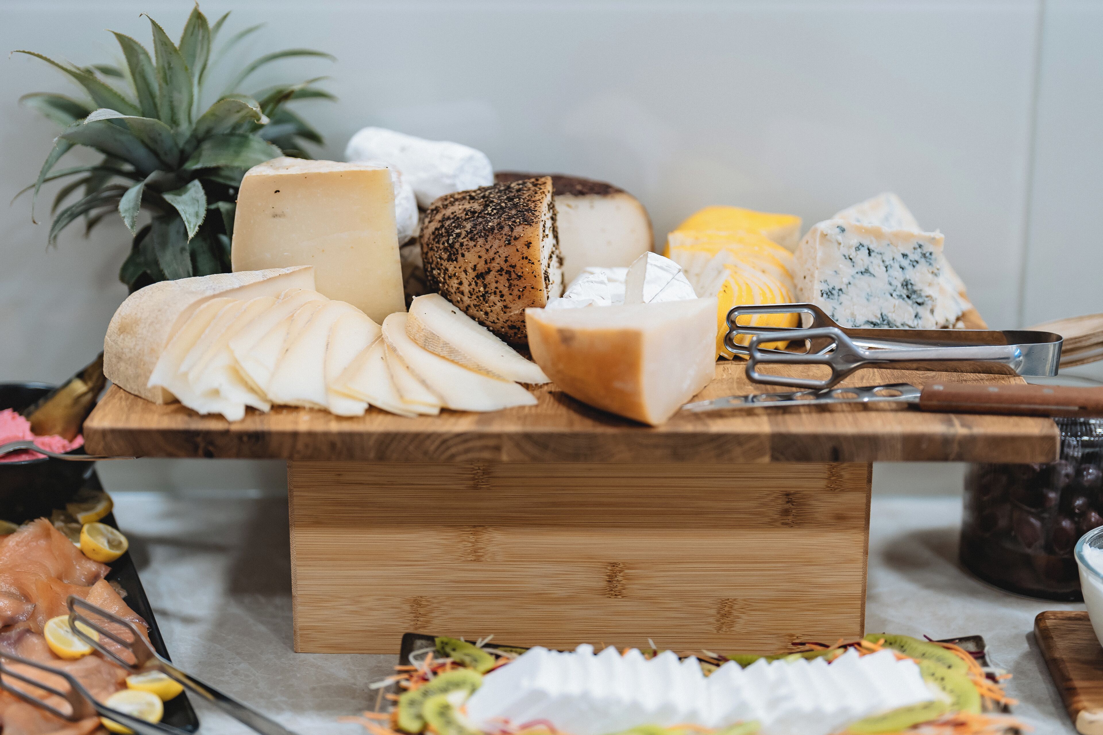 Una tabla de madera con varios quesos, una piña y un cuchillo.