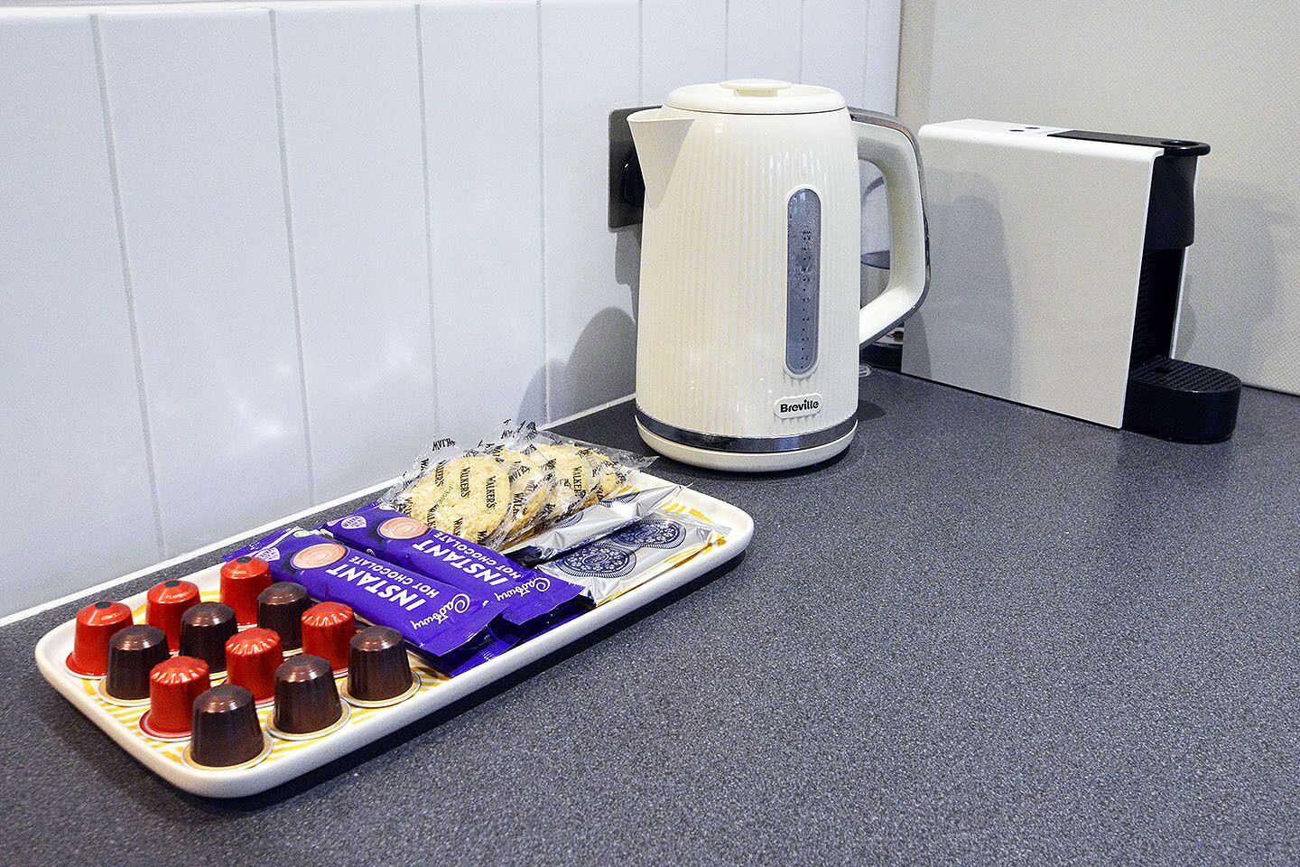 Un plan de travail de cuisine avec une bouilloire Breville, un plateau de chocolat chaud et un paquet de café instantané.