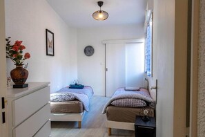 A narrow room with two beds, a small table, a vase with flowers, and a ceiling light. - LA Stationt2confortwifihypercentre (Lourdes)