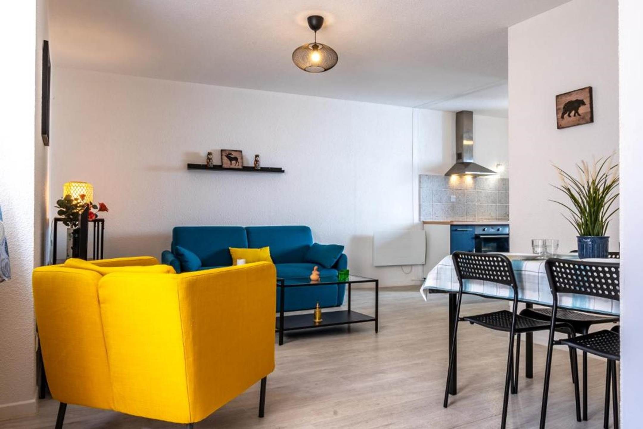 A modern living room with a blue sofa, a yellow armchair, and a dining area with a table and chairs.