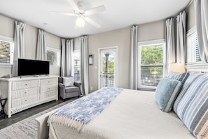 Quarto com cama, televisão, cómoda, cadeira e janela com persianas.