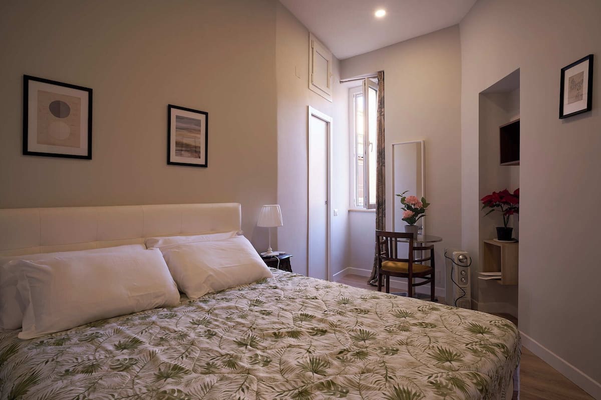 A bedroom with a bed, a nightstand, a chair, a small table, and a mirror.