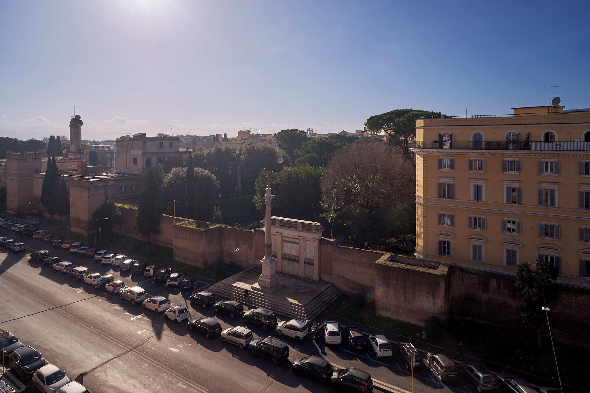 A cityscape with a row of parked cars, a prominent monument, and a building with multiple windows.