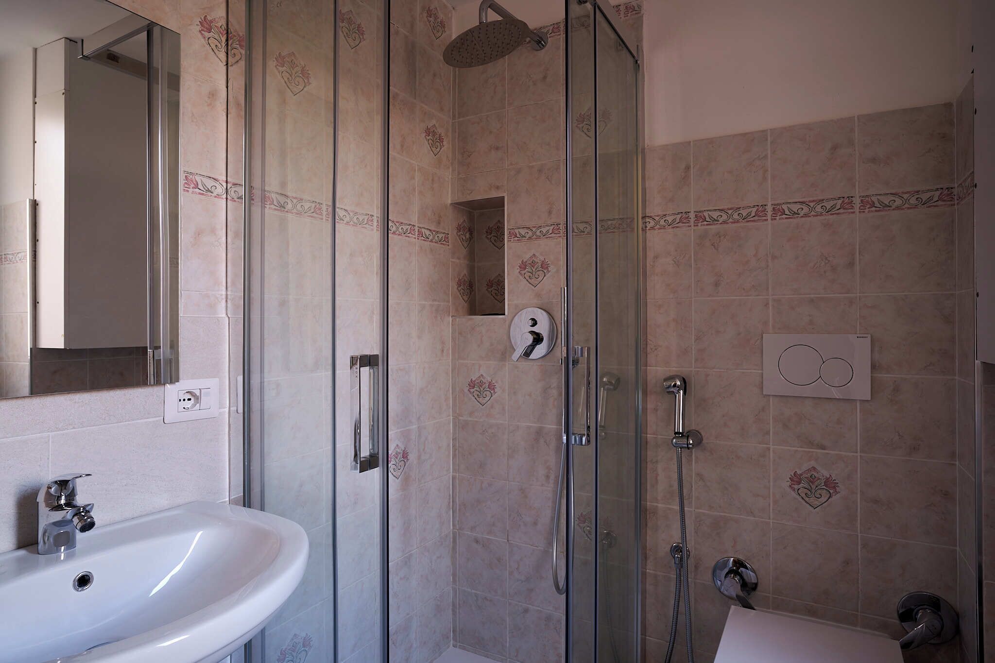 Een badkamer met een douchecabine van glas, een wastafel en een spiegel.