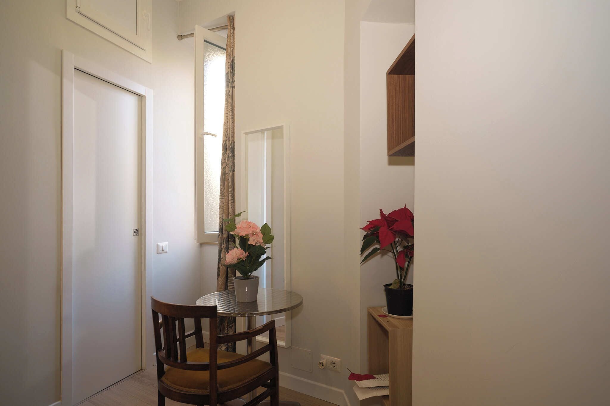 A hallway with a closed door, a small round table with a chair, and a potted plant on a stand.