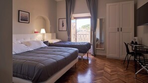 Habitación de hotel con dos camas, un escritorio, una silla, un televisor y un balcón con cortinas.