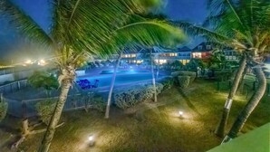 Una vista notturna di un resort con piscina, palme e edifici illuminati.