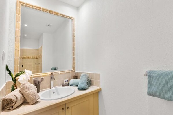 A bathroom with a white sink, beige vanity, and a large mirror. There are towels and a plant on the vanity.