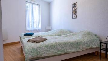 A bedroom with two beds, a window with curtains, a chair, and a wall-mounted decoration.