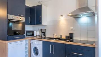 A compact kitchen with a washing machine, microwave, coffee maker, and a stainless steel range hood.