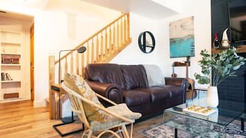 Ein Wohnzimmer mit einer Ledersofa, einem Holzstuhl, einem Glastisch, einer Treppe und einem Bücherregal.