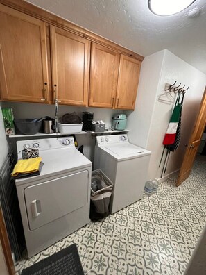 A compact laundry area with wooden cabinets, a washing machine, a dryer, and a small trash bin.