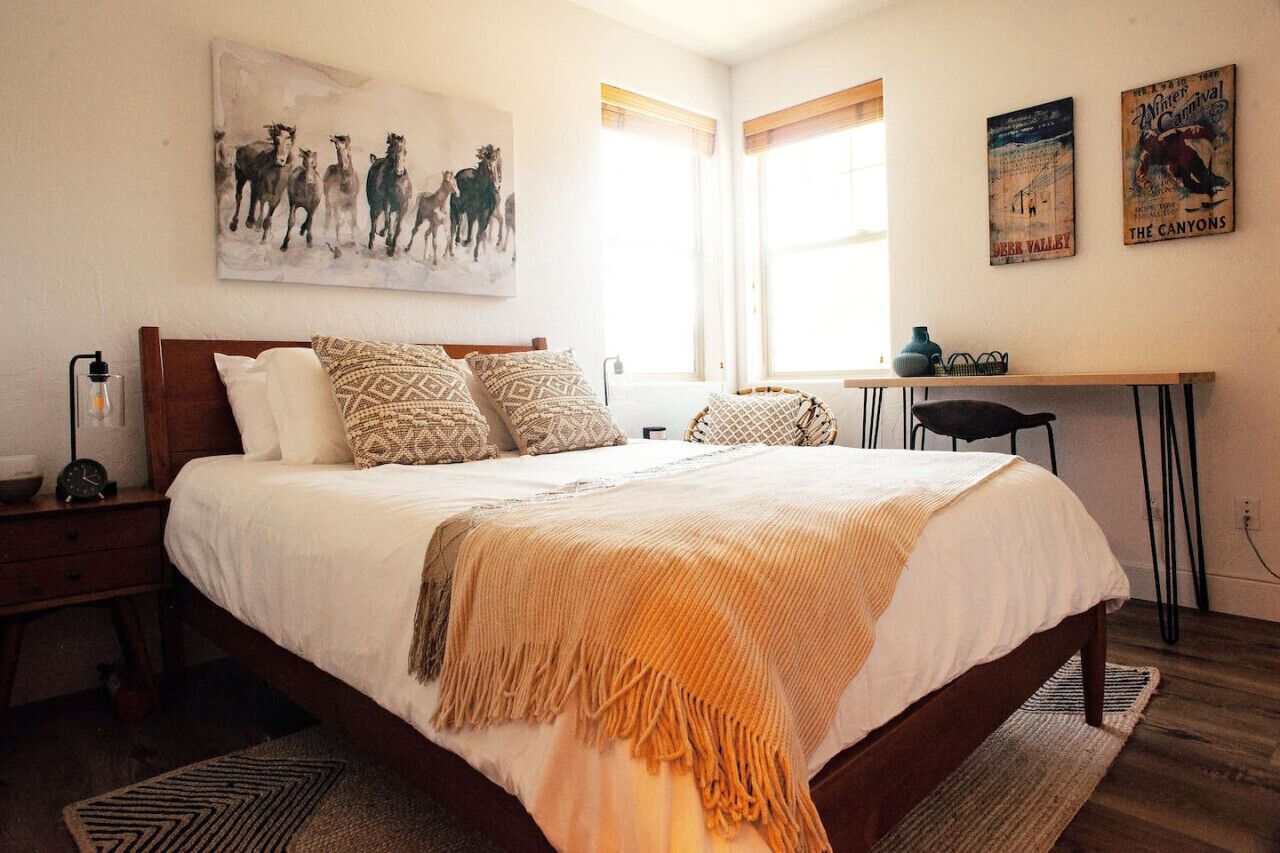 A bedroom with a large bed, a desk, and a chair. There are posters on the wall and a window with blinds.