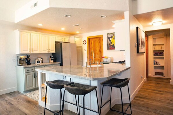 A modern kitchen with a large island, bar stools, and a dining area with a wooden door.