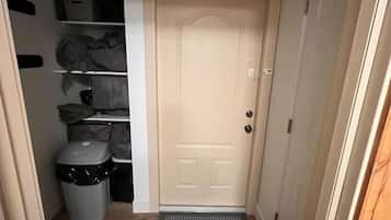 Un pasillo con una puerta, un bote de basura y estantes con objetos.