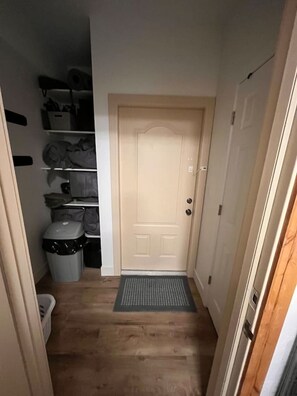 A hallway with a door, a trash bin, and shelves with items.