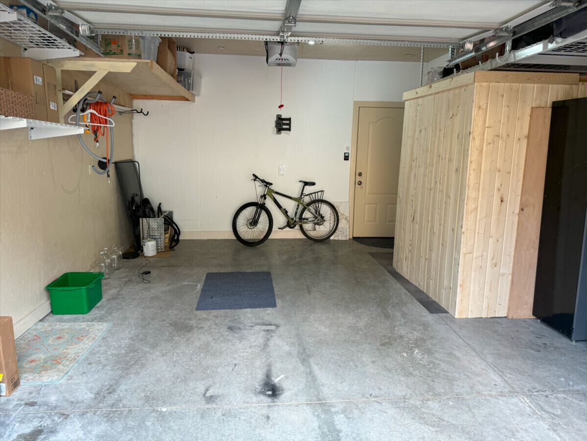 A garage with a bicycle, a green storage bin, and a mat on the floor.