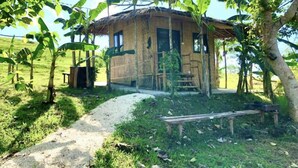 Una casa de madera rústica con tejado de paja, rodeada de exuberante vegetación y palmeras de plátano.