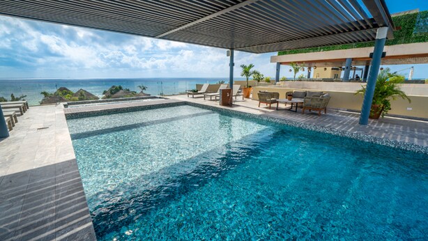 A clear blue pool with lounge chairs and a view of the ocean. - Jojo - 1 Bedroom Condo At Singular Joy (Playa del Carmen)