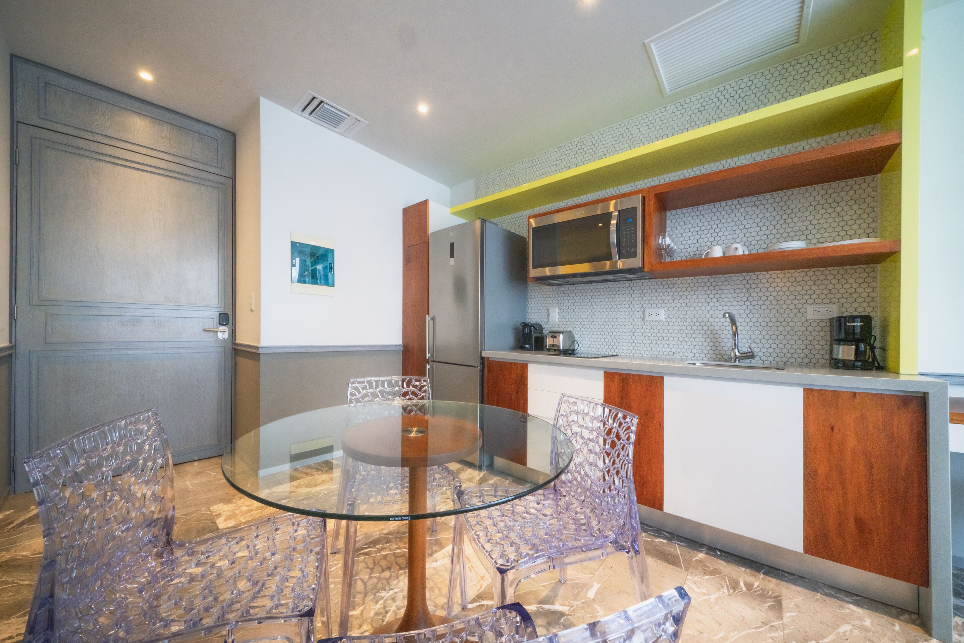 A modern kitchen with a glass dining table and chairs, a built-in microwave, and wooden cabinets.