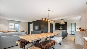Une cuisine moderne avec un îlot central, un coin repas avec une table et des bancs en bois, et un canapé gris dans l’espace salon.