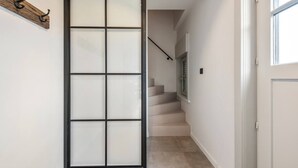 Un couloir avec une cloison en verre dépoli, un escalier et une porte dotée d’une fenêtre.