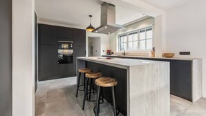 Une cuisine moderne dotée d’un îlot central, de tabourets de bar et d’une grande fenêtre qui laisse entrer la lumière naturelle.