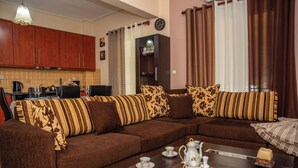 Ein Wohnzimmer mit braunem Sofa, einem Couchtisch mit Teeservice und einer Küche im Hintergrund.