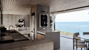 Eine moderne Küche mit Betondecke, einem großen, schwarzen Kunstwerk und Blick auf das Meer.