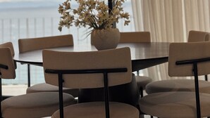 Ein Essbereich mit Tisch und Stühlen, einer Blumenvase und Blick zum Himmel durch große Fenster.