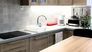 Une cuisine moderne avec des armoires en bois, une hotte de cuisinière en acier inoxydable, un four encastré, un évier avec un robinet et un plan de travail sur lequel se trouvent un grille-pain et une machine à café.
