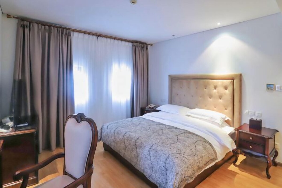 A hotel room with a large bed, a wooden chair, a bedside table, and a television.