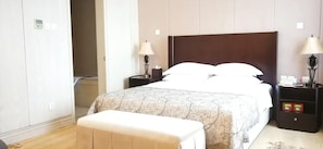 Una habitación de hotel con una cama grande, mesitas de noche, un banco y un armario.