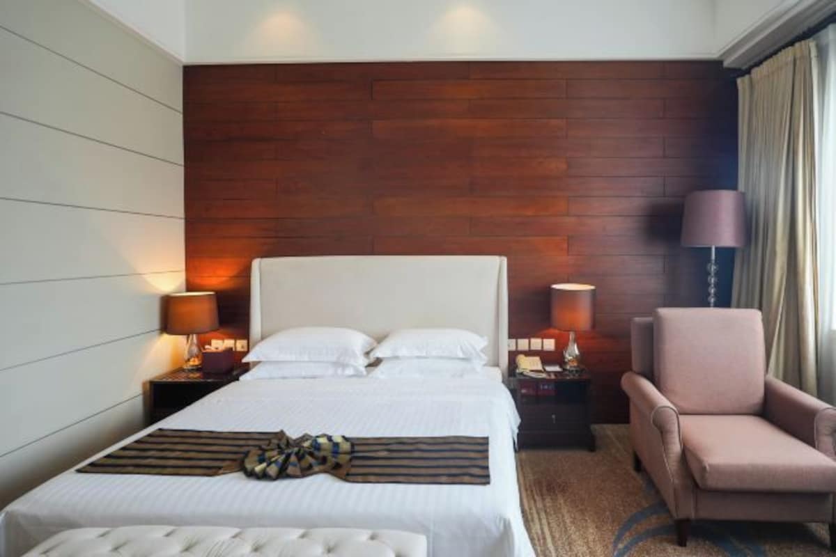 A hotel room with a large bed, two bedside tables with lamps, a chair, and a wooden accent wall.