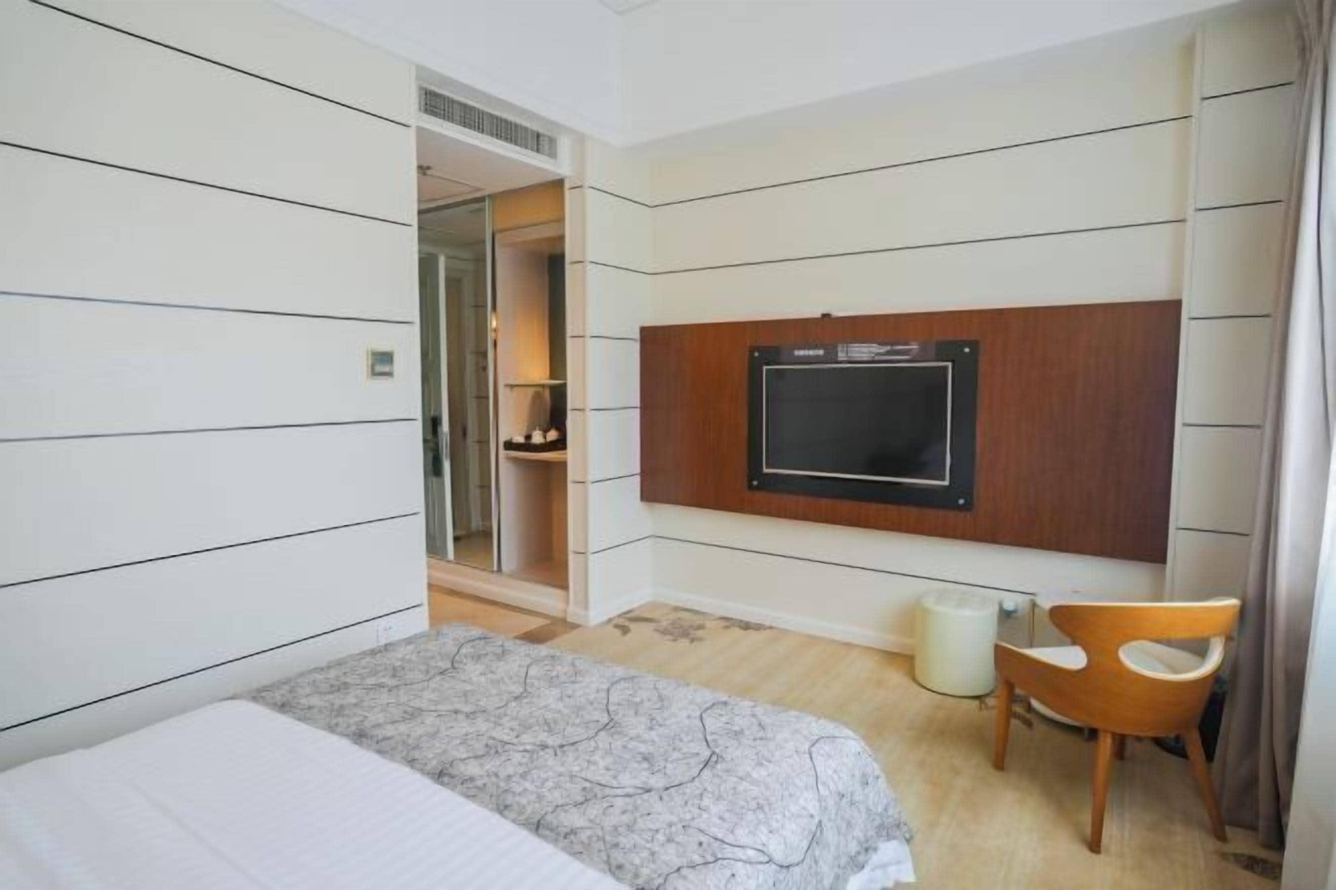 Habitación de hotel con cama, televisor montado en la pared, una silla y una mesita.