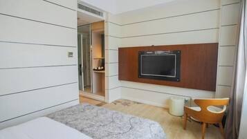Habitación de hotel con cama, televisor montado en la pared, una silla y una mesita.