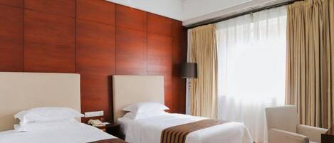 A hotel room with two beds, a desk, a chair, and a large window with curtains.