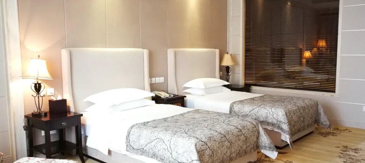 Une chambre d’hôtel avec deux lits, des lampes de chevet, une table de chevet et une fenêtre avec des stores.