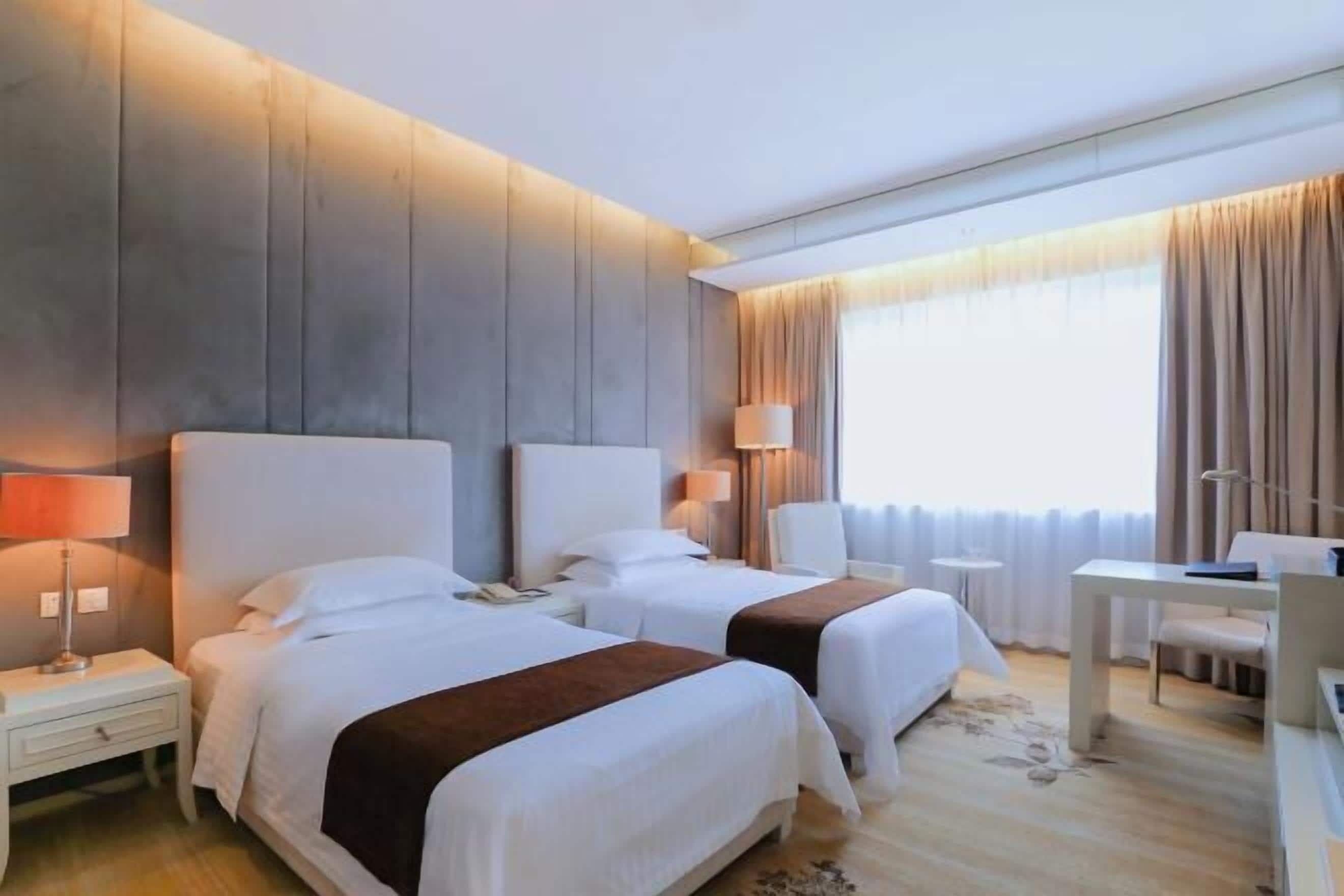 A hotel room with two beds, a desk, and a chair.
