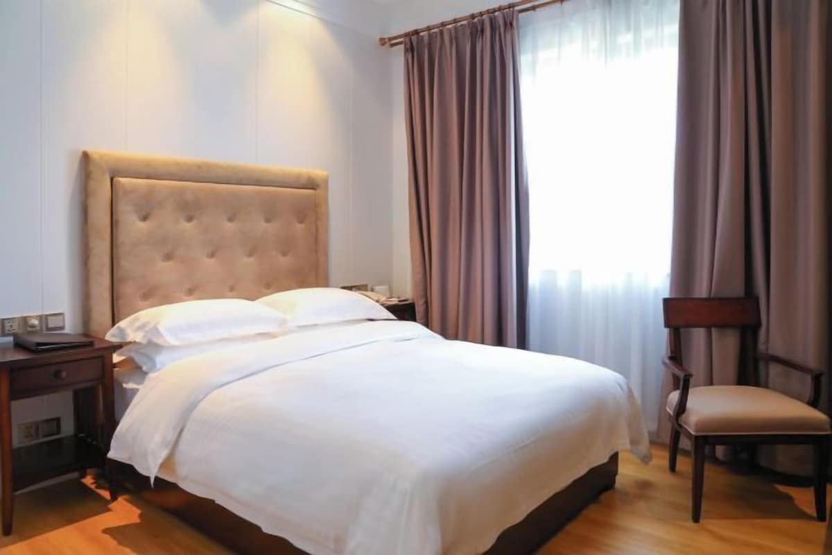 A hotel room with a large bed, a nightstand, a chair, and a window with curtains.