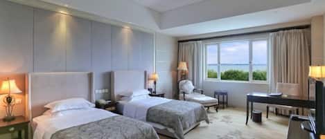 Een hotelkamer met twee bedden, een bureau, een stoel, een lamp en uitzicht op zee.
