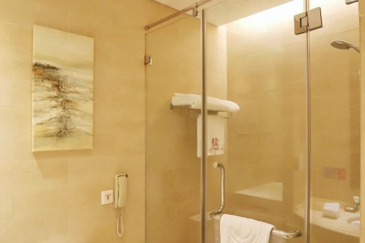 Una ducha con mampara de vidrio, un perchero, un teléfono de pared y un cuadro.