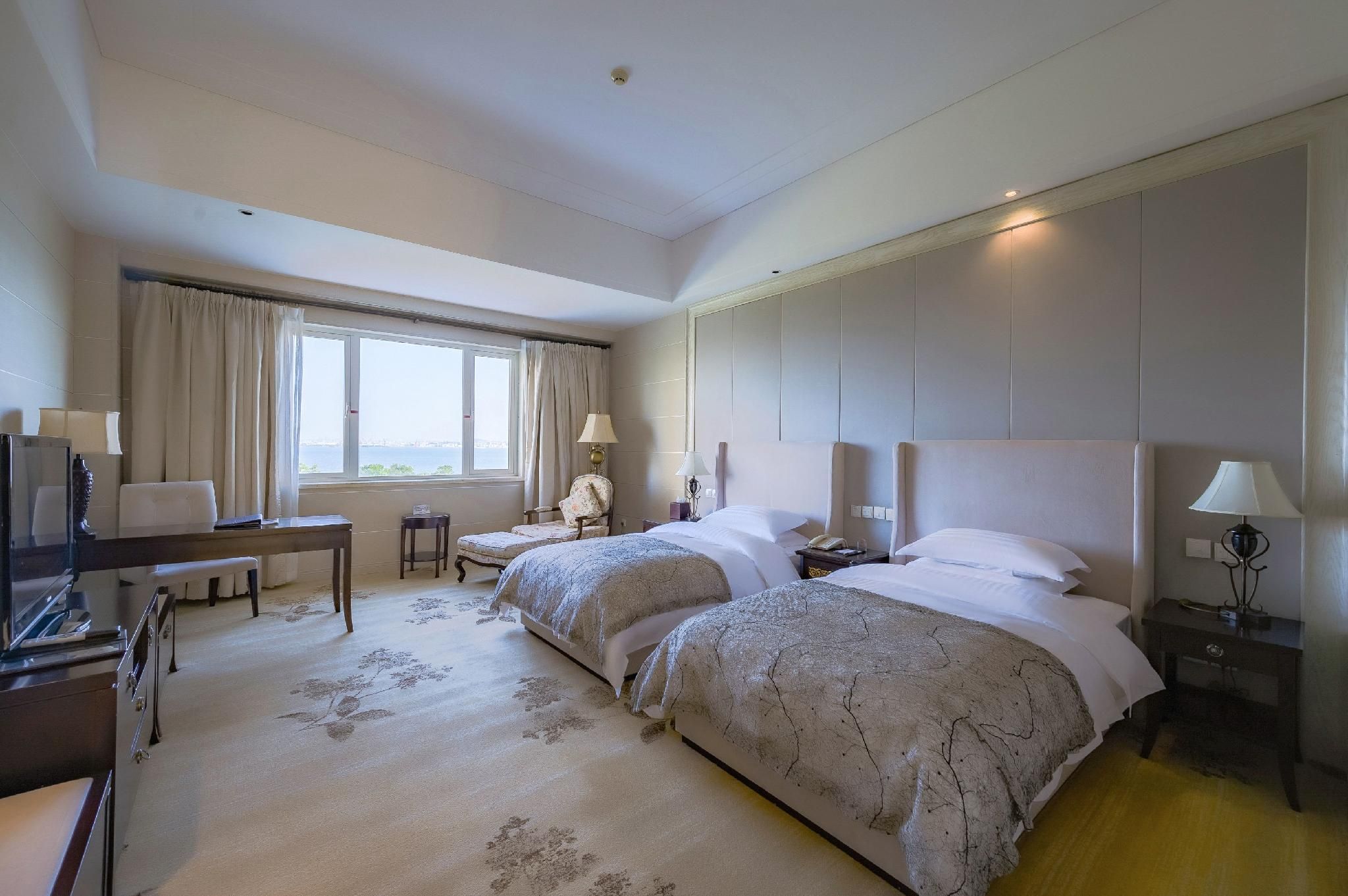 Ein Hotelzimmer mit zwei Betten, einem Schreibtisch, einem Sessel, einem Fernseher und Blick auf das Meer.