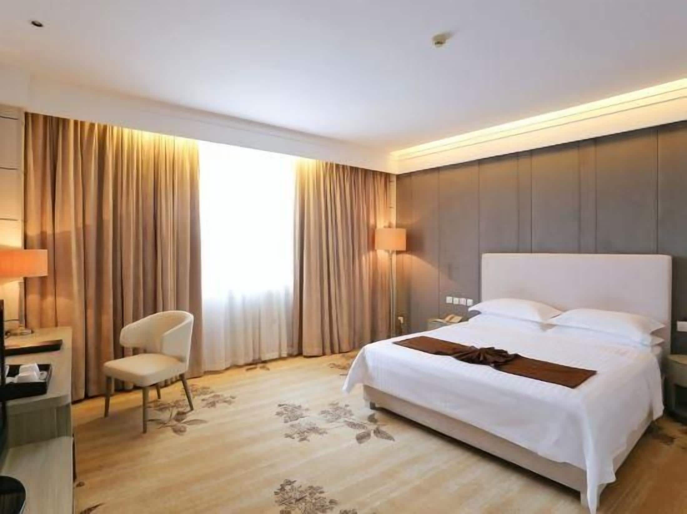 Habitación de hotel con una cama grande, un escritorio, una silla y una ventana con cortinas.