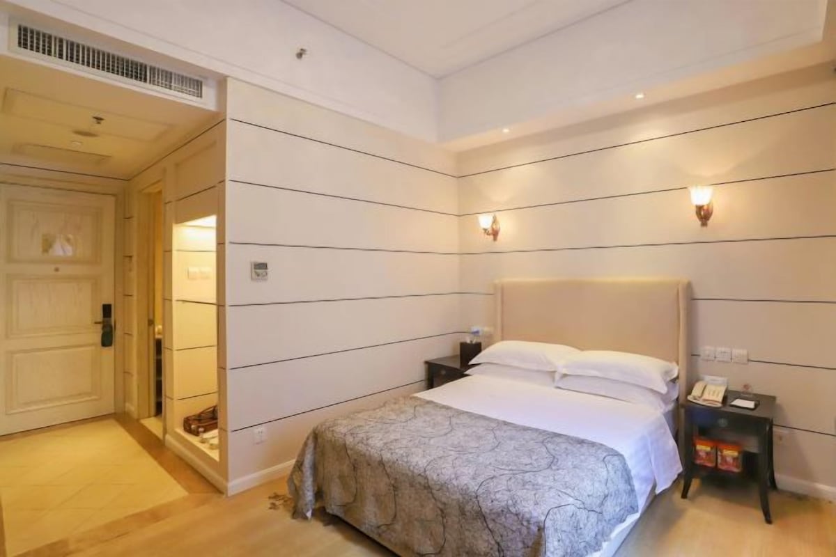 A hotel room with a large bed, bedside tables, a wardrobe, and a door.