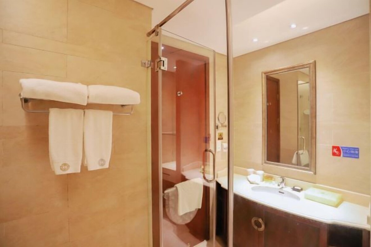 A hotel bathroom with a glass shower enclosure, a sink with a mirror, and two towels on a rack.